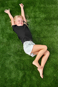 漂亮的金发女孩闭着眼睛躺在绿色的草地上伸展。