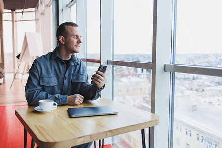 微笑的男经理坐在咖啡馆里使用手机小工具，通过在线应用程序订购送货服务，咖啡馆内免费 4g 无线网络，快乐的自由职业者在手机上发短信