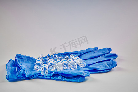 七个样机安瓿，装有透明液体，蓝色一次性手套，隔离在白色。