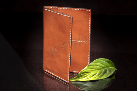 深色背景上的皮革棕色开放钱包和绿叶。