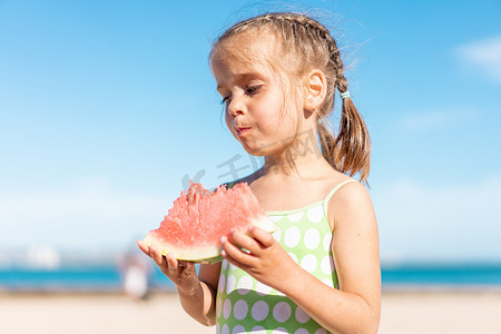 吃女孩西瓜摄影照片_有趣的小女孩在海洋海滩吃西瓜阳光明媚的夏日。