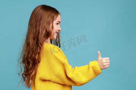 可爱摄影照片_可爱迷人的小女孩竖起大拇指的侧视图肖像，显示出认可的手势。