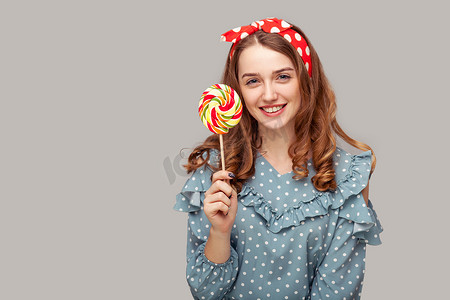 宣传海报音乐摄影照片_漂亮的海报女孩荷叶边衬衫拿着甜螺旋糖果看着相机，微笑着美味的糖果