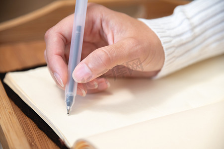 家中木桌上的皮革记事本上用凝胶黑笔书写的女手特写