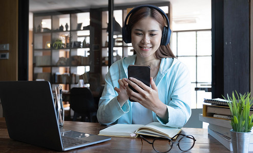 美丽的千禧一代亚洲女大学生用现代无线耳机和智能手机听音乐。