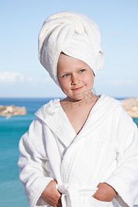 海背景上头戴毛巾、身穿白色浴袍的小女孩