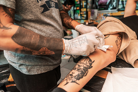 皮肤喷雾摄影照片_拉丁纹身师对客户的腿进行消毒，以继续捕捉艺术