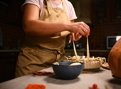穿着米色厨师围裙的特写家庭主妇，用松脆的糕点格子装饰感恩节南瓜苹果派。