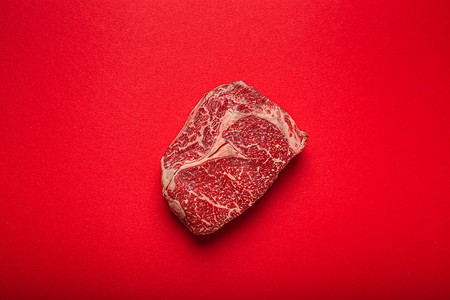 从上面摄影照片_生肉牛肉优质切牛排肋眼从上面干净的红色背景，牛排概念横幅极简主义