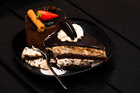 巧克力慕斯配草莓、巧克力棒和奶油芝士蛋糕配巧克力饼干，黑色盘子上的奶油饼干。