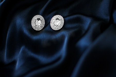 丝绸珠宝摄影照片_深蓝色丝绸背景的豪华钻石耳环，节日魅力珠宝礼物