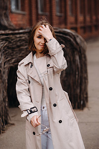 灰色外套摄影照片_一个穿着灰色外套的快乐时尚女孩在城市里走来走去