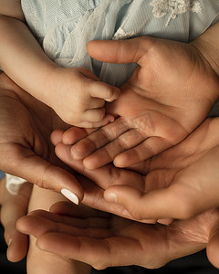 父亲孩子手牵手摄影照片_特写：慈爱的爸爸妈妈和孩子手牵手在地板上，手掌向上，表达亲密和团结，有爱心的父母与孩子并肩作战，表现出奉献、支持和联系。
