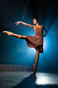 优雅的芭蕾舞演员穿着古典或现代芭蕾舞元素，在黑暗中用泛光灯背光跳舞。