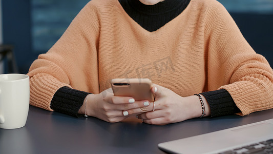 快乐的女人在办公桌前用智能手机浏览互联网