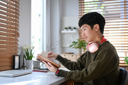 秋日时光摄影照片_冷静的亚洲男子戴着无线耳机阅读最喜欢的文学作品，在冬季周末度过休闲时光