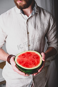 切片水果摄影照片_留胡子的男人手里拿着一半红西瓜