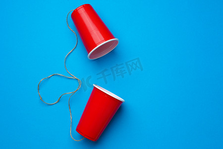 蓝色背景上用绳子连接的两个红纸杯，玩具电话