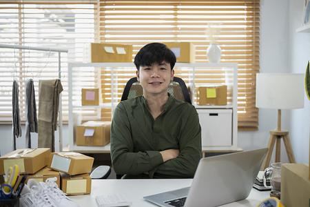 亚洲人创办小企业主，坐在家里办公室里，家里办公室里放着纸箱。