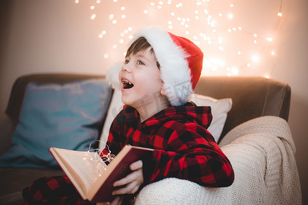 一个戴着圣诞帽的男孩正在生活方式沙发上看书。