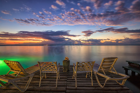 等待日出摄影照片_木码头上空荡荡的躺椅和椅子，等待海滩上的日出。
