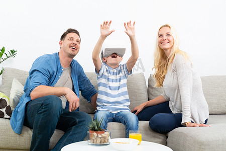 快乐的家庭在家里的客厅沙发上使用虚拟现实耳机玩游戏