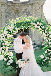 新娘和新郎站在石墙喷泉前的婚礼拱门附近