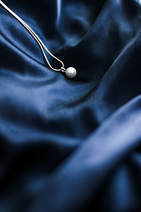 深蓝色丝绸背景上的豪华白金珍珠项链，假日魅力珠宝礼物