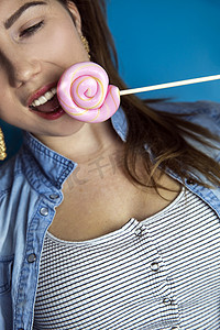 蓝色背景、糖果、糖和不健康食品概念上，一个漂亮女孩的肖像，上面有彩色粉色旋转棒棒糖硬糖