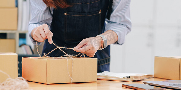 开办小企业，中小企业主，女企业家正在用绳子系箱子来包装产品在线订购准备包装一盒商品出售给客户，中小企业在线经营理念