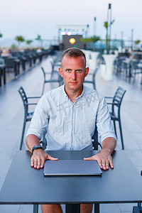 一位成功的商人在酒店露台上使用笔记本电脑工作，并在异国情调的度假胜地度假时抽出时间远程管理员工。