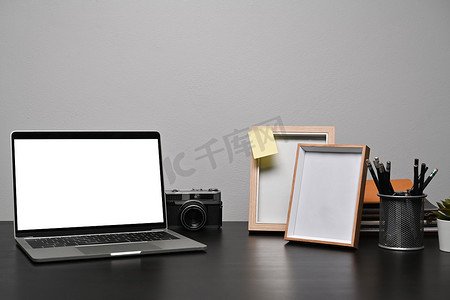 黑桌上有白色屏幕、相机和空相框的笔记本电脑。