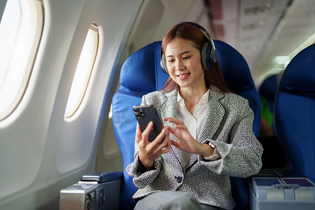 一位成功的亚洲女商人在飞机上的肖像坐在商务舱座位上，在飞行过程中使用智能手机播放音乐，relex 概念