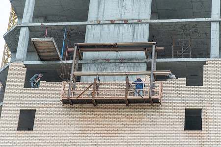 高空升降平台摄影照片_俄罗斯莫斯科，05,10,2021：建筑物的修复、重建和维修。建筑工人站在升降平台上铺砖。房屋修复施工现场