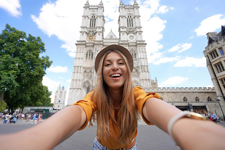 年轻的旅行者女孩在伦敦与威斯敏斯特大教堂哥特式教堂合影。