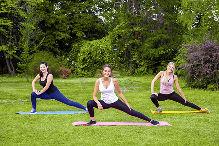 黏糊糊的摄影照片_一群美丽健康、黏糊糊的女人在公园绿草的垫子上做运动，伸展双腿，带着露齿微笑看着镜头。