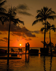 毛里求斯度假期间，带棕榈树的日落热带泳池，一对男女在带棕榈树的泳池边看日落