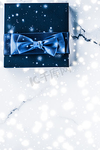 礼盒展示摄影照片_冬季节日礼盒，配有蓝色丝绸蝴蝶结、大理石背景上的雪花，作为豪华美容品牌的圣诞和新年礼物，平铺设计