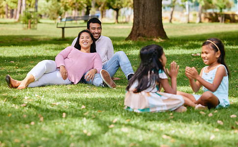 一对幸福的亚洲夫妇一起躺在外面的草地上，慈爱的父母与他们的小女儿玩游戏享受美好时光。