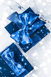 美容品牌摄影照片_冬季节日礼盒，配有蓝色丝绸蝴蝶结、大理石背景上的雪花，作为豪华美容品牌的圣诞和新年礼物，平铺设计