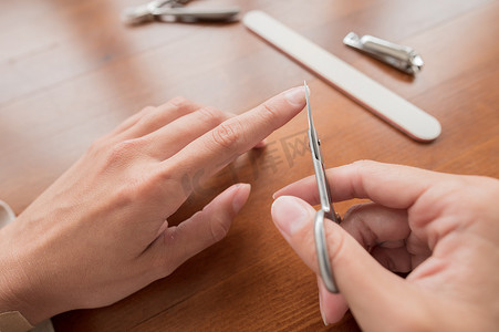 白种人年轻女子的手的特写，她正在做美甲剪刀，在家里用美甲用品剪指甲。