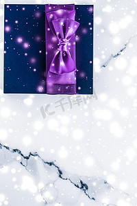 带紫色丝弓的寒假礼盒，大理石背景上闪闪发光的雪花，作为豪华美容品牌的圣诞和新年礼物，平面设计