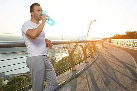一位帅气迷人的中年白人肌肉男的腰长肖像，黎明时分在城桥跑步机上晨跑后喝水的运动员