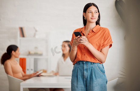 一位年轻的西班牙裔女商人在办公室里一边用手机发短信一边思考，背景是她的同事。