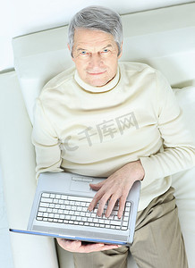 家里的老人，沙发上放着笔记本电脑，抬头看