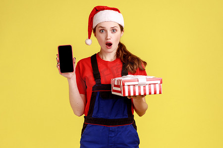 瑞创广告摄影照片_震惊而兴奋的快递女性拿着礼品盒和手机，上面有空的广告展示。