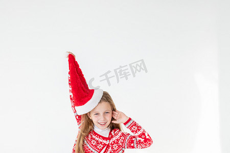 快乐的女孩跳舞的画像，穿着红色圣诞毛衣和孤立在白色背景上的圣诞老人帽子。穿着圣诞马鹿毛衣的年轻白种人快乐微笑的金发女孩很开心。