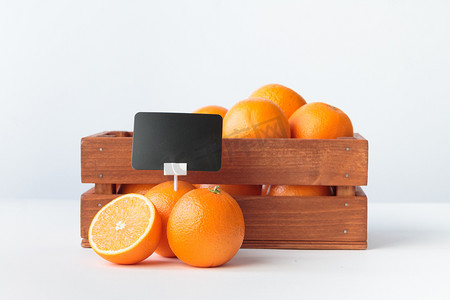 特写商品摄影照片_木箱里有价格持有人的橙子