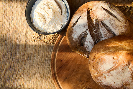 bre摄影照片_新鲜出炉的自制全麦面包和杂粮面包，放在木板上，上面有小麦小穗，还有白面粉