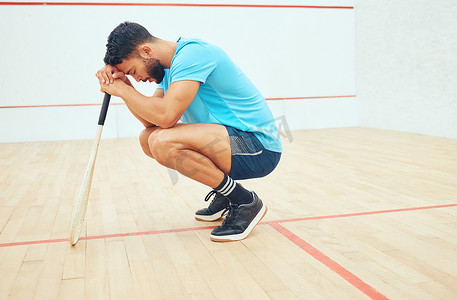 一名不知名的运动壁球运动员在球场上打完比赛后蹲下，感到悲伤和压力。